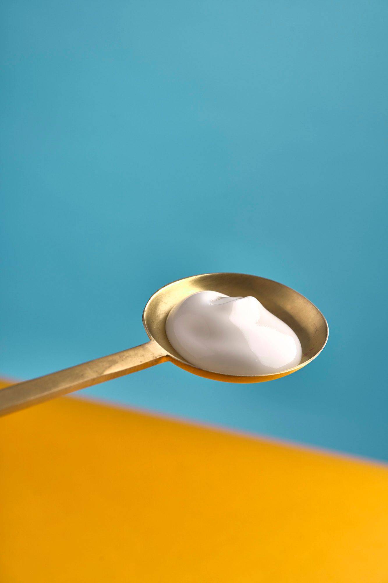griechischer-joghurt griechischer joghurt auf einem messinglöffel mit gelbem und blauem hintergrund