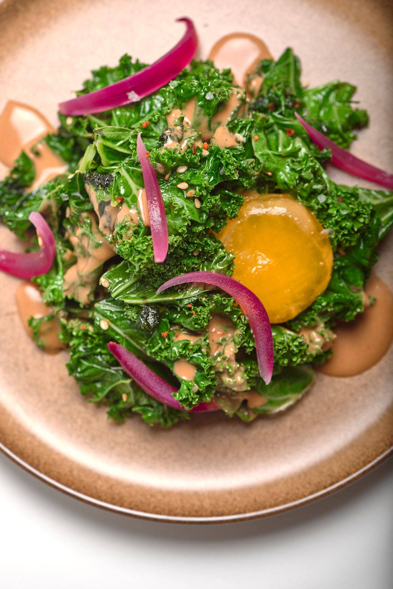 kale-salad-with-miso-egg-yolk-and-rosehip kale salad with miso egg yolk and rosehip on a brown ceramic plate with white background
