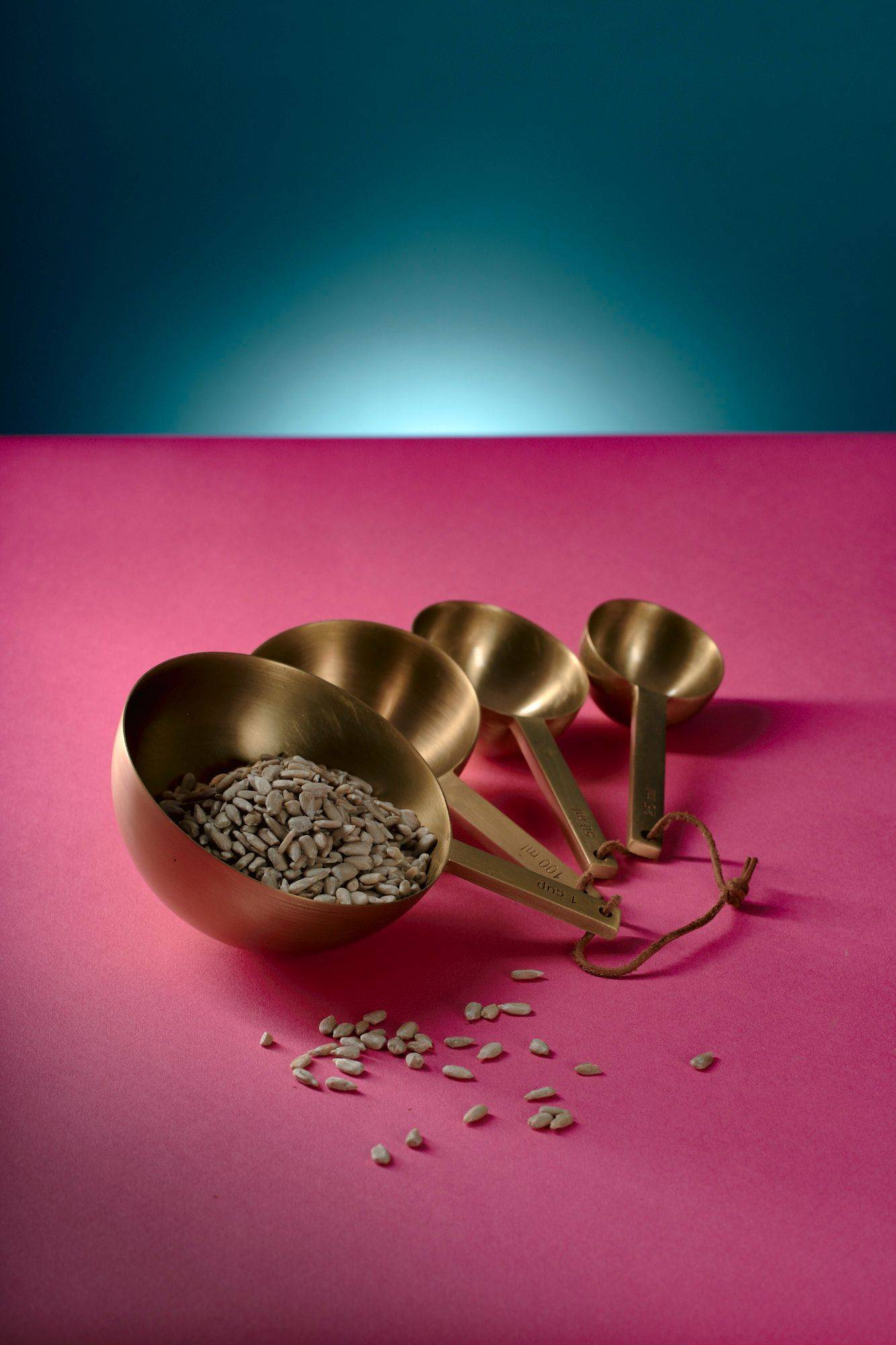 sunflower-seeds sunflower seeds in brass measuring spoons with pink and blue background