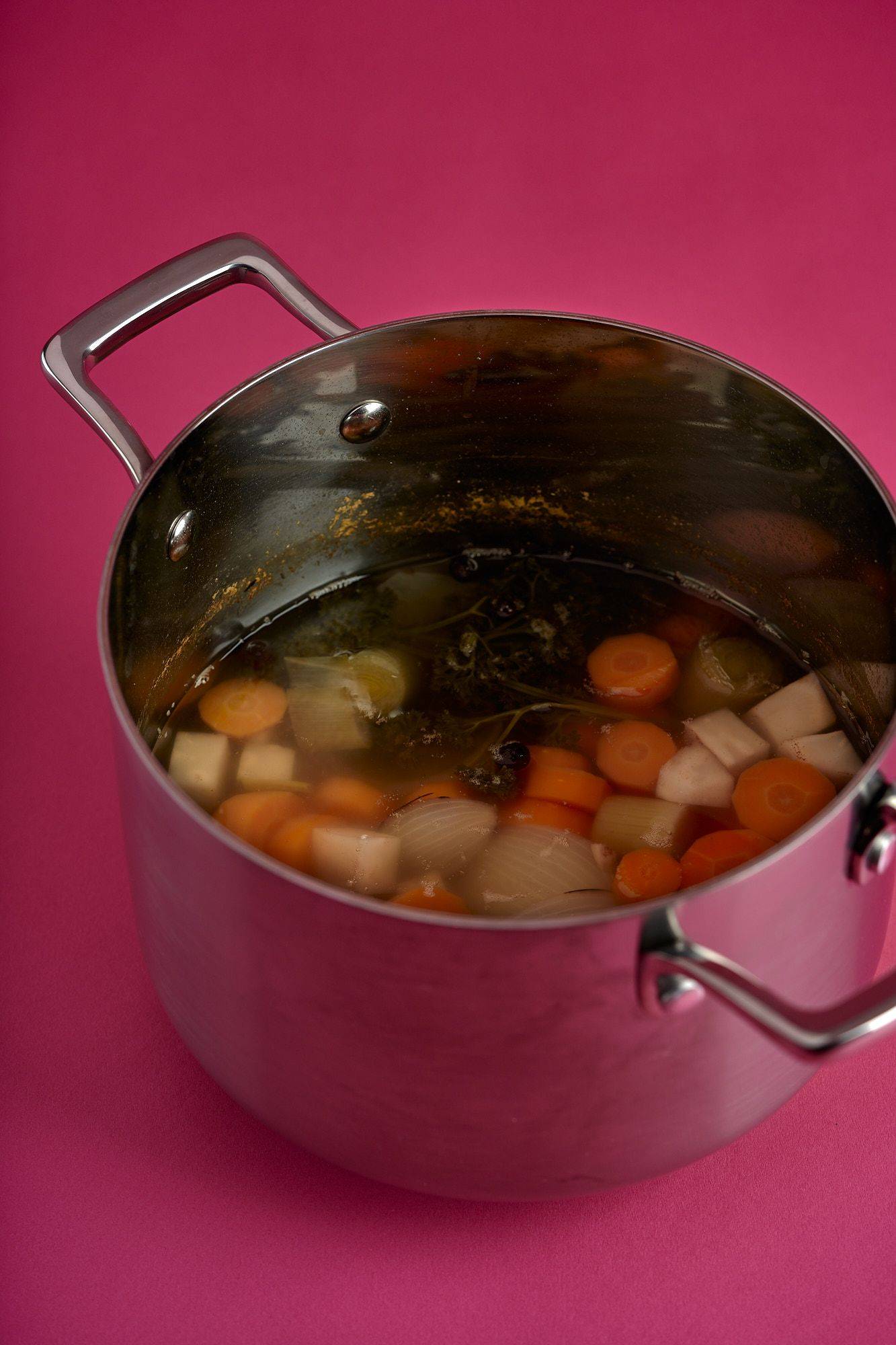 vegetable-broth a silver pot with vegetable broth on pink background