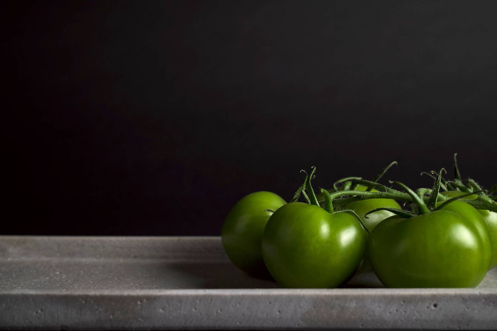 green-tomatoes five green tomatoes on a concrete plate on black background