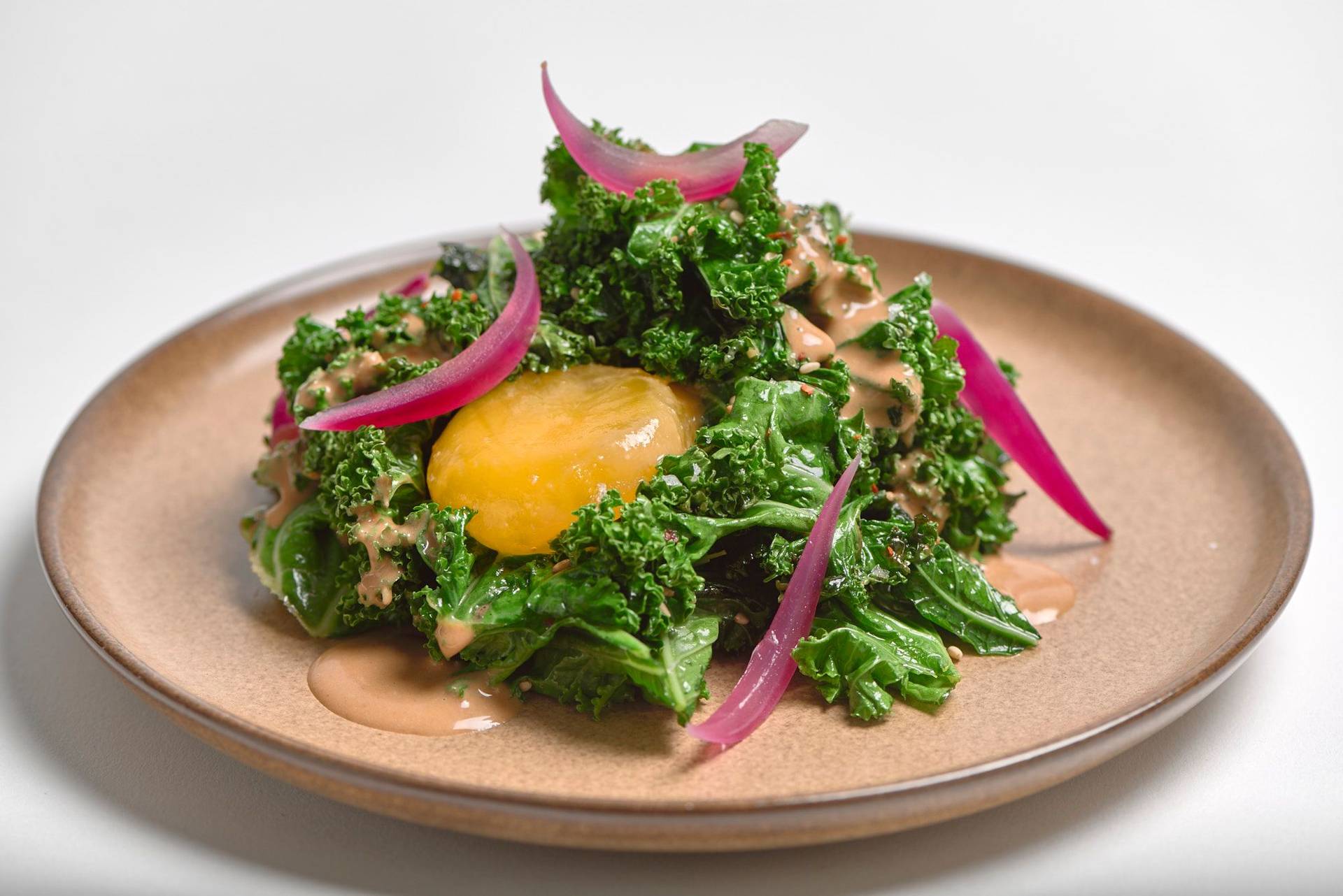 kale-salad-with-miso-egg-yolk-and-rosehip kale salad with miso egg yolk and rosehip on a brown ceramic plate with white background