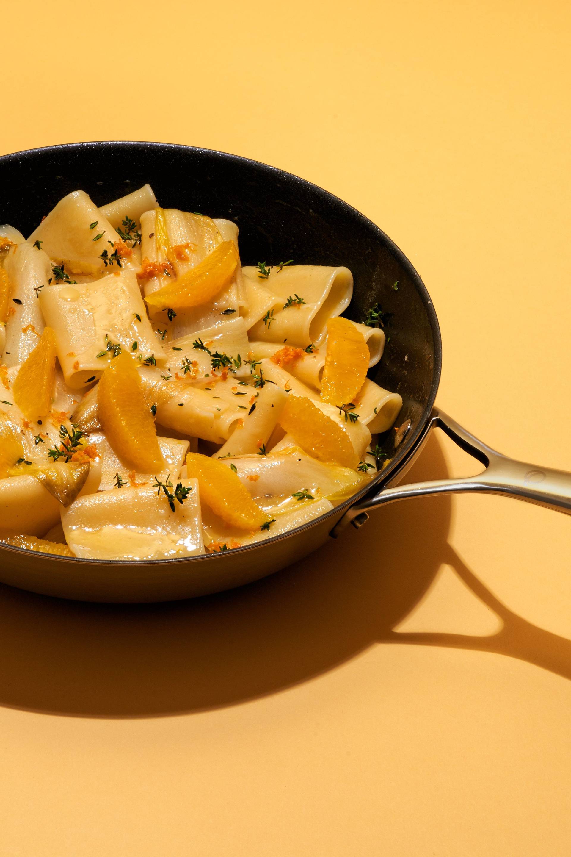 vegetarian-one-pot-pasta-with-chicory-and-orange an olav pan with vegetarian one pot pasta with chicory and orange on yellow background