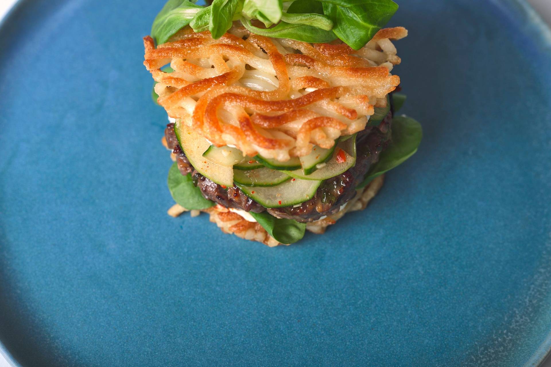 bulgogi-beef-burger-with-cucumber-kimchi bulgogi beef burger with cucumber kimchi and udon noodle buns on a blue ceramic plate