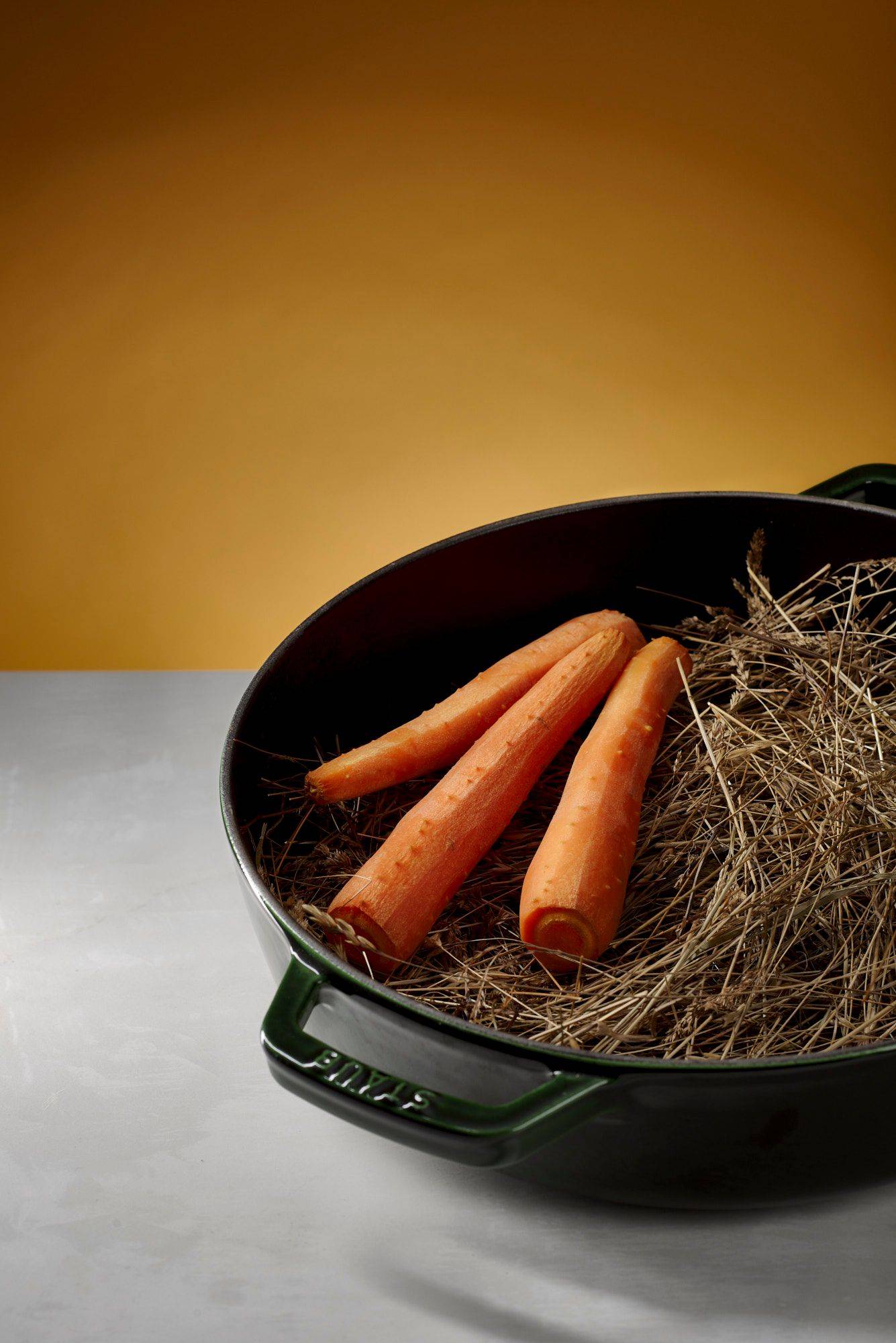 carrots-in-hay carrots in hay with green staub cast iron pot with white sapienstone top and yellow background