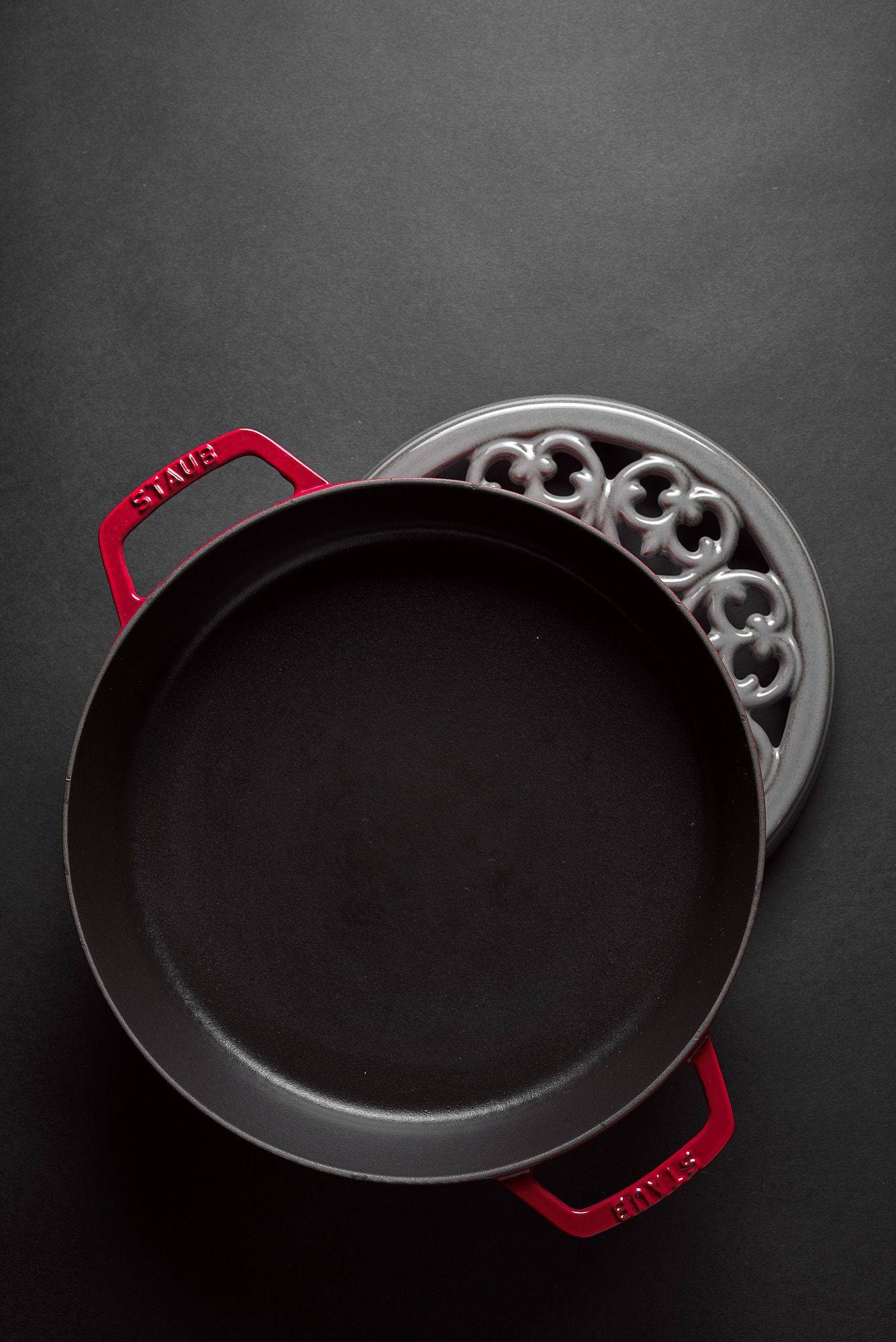 staub-la-cocotte-cast-iron-pots red staub la cocotte cast iron pot and coaster on black background