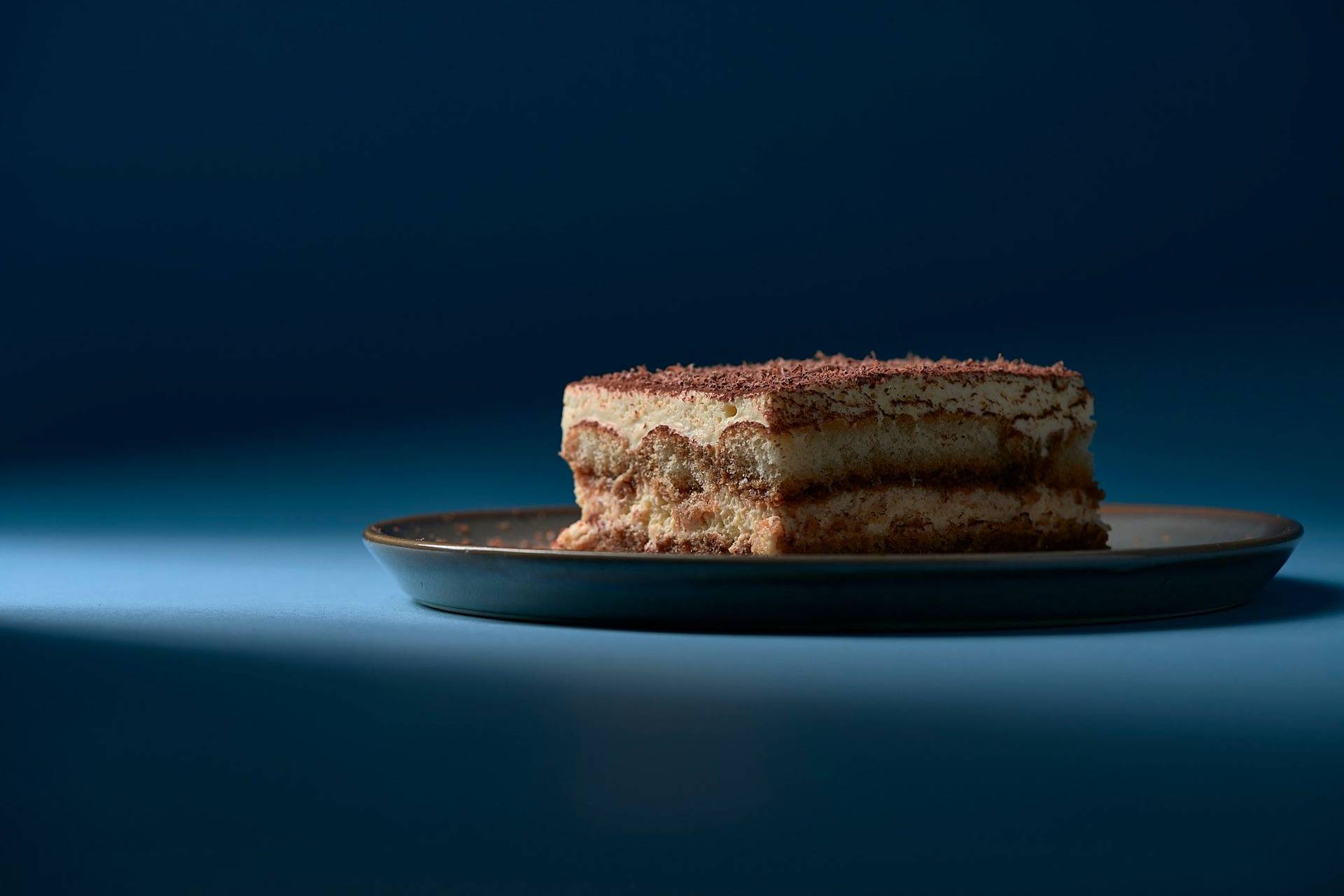 original-italienisches-tiramisu-dessert original italienisches tiramisu dessert auf grauem teller mit blauem hintergrund