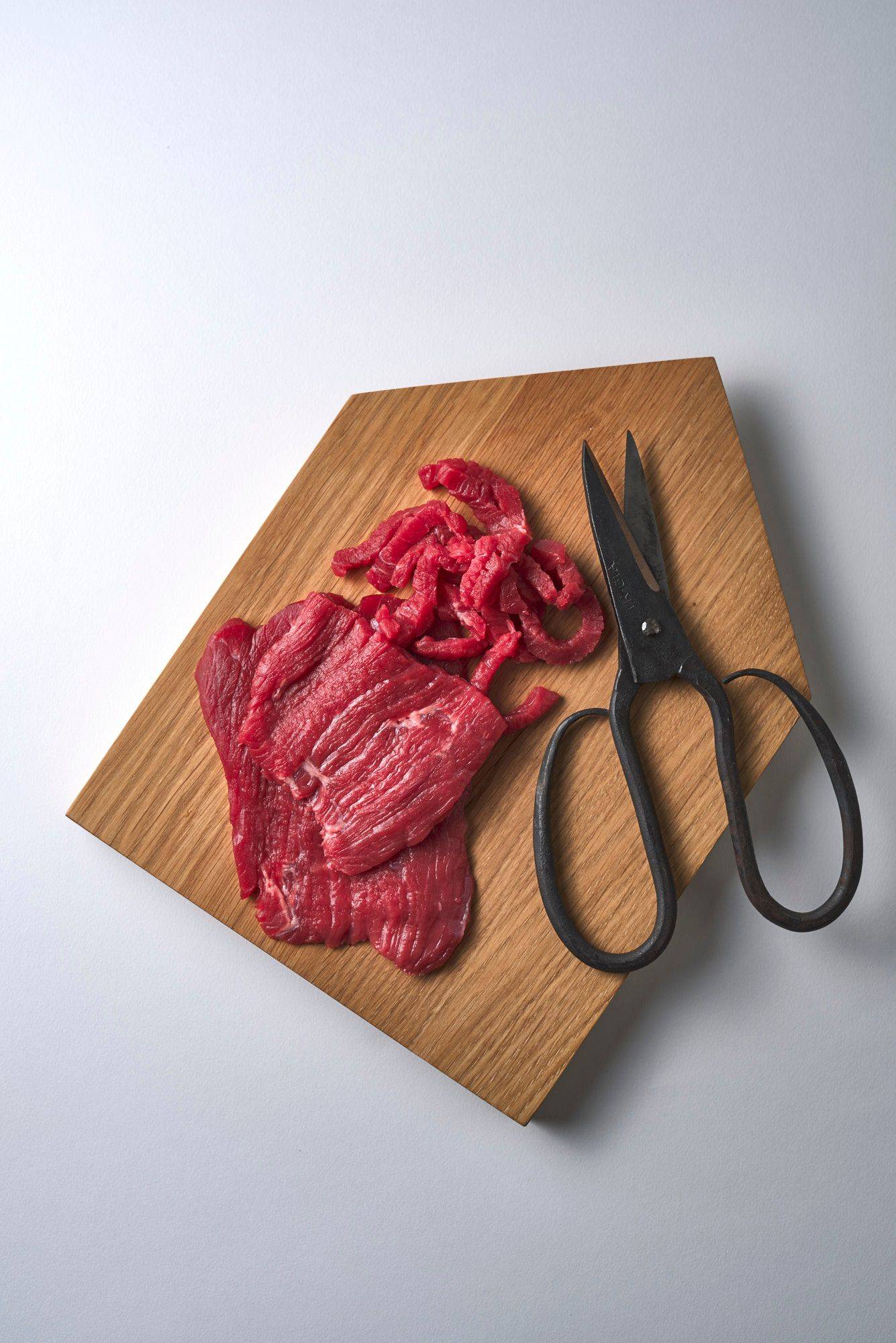 beef beef on a wooden tray with scissors on white background