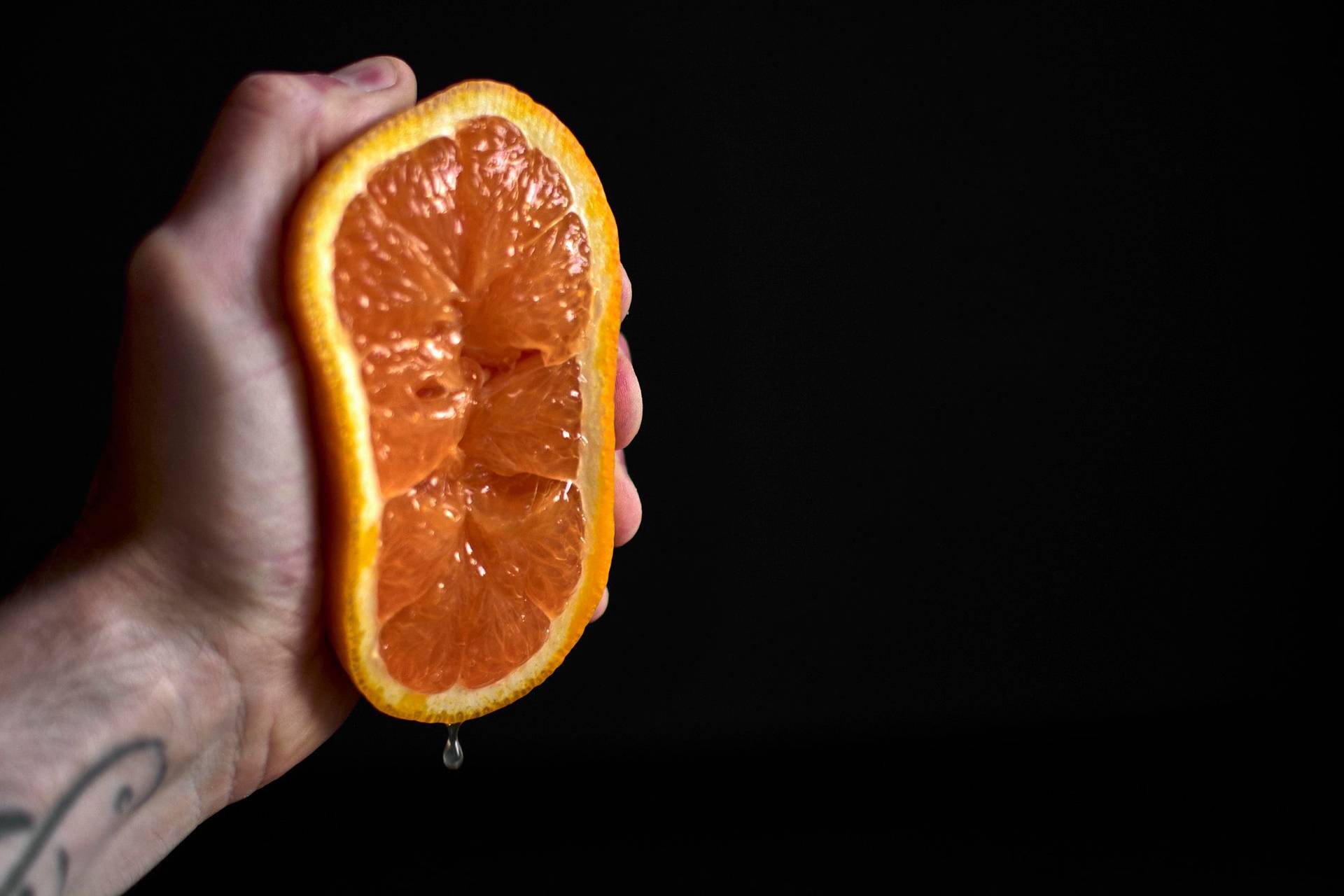 orange hand squeezing an orange on black background