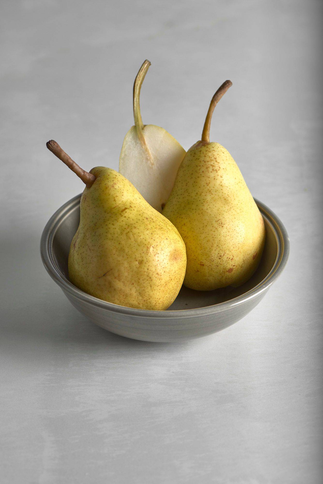 pears three pears in a gray ceramic bowl on a white stone table