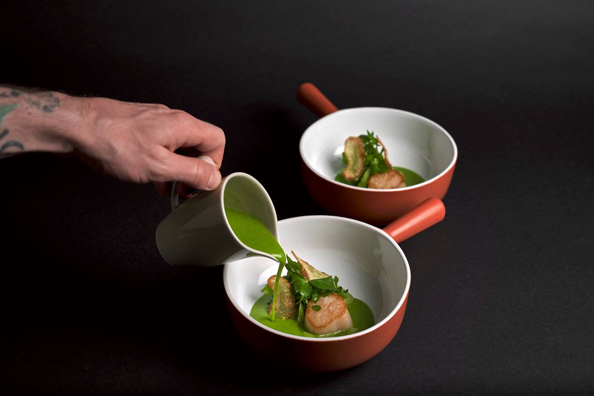 scallops-verde two bowls of seared scallop with potato, wild garlic and sorrel sauce and chickweed on black background