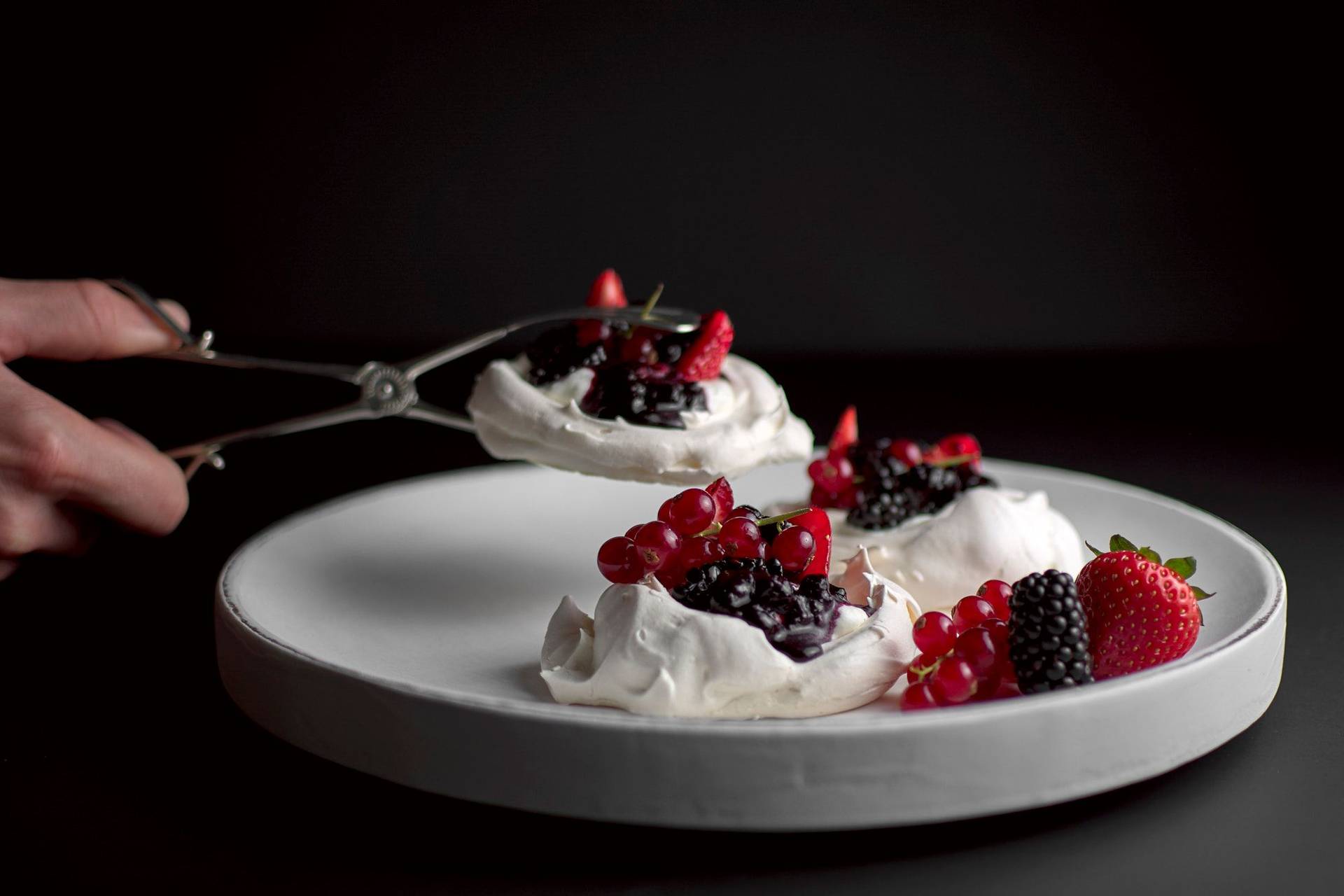pavlova-with-berries-and-salted-cream pavlova with berries and salted cream on a white plate with black background
