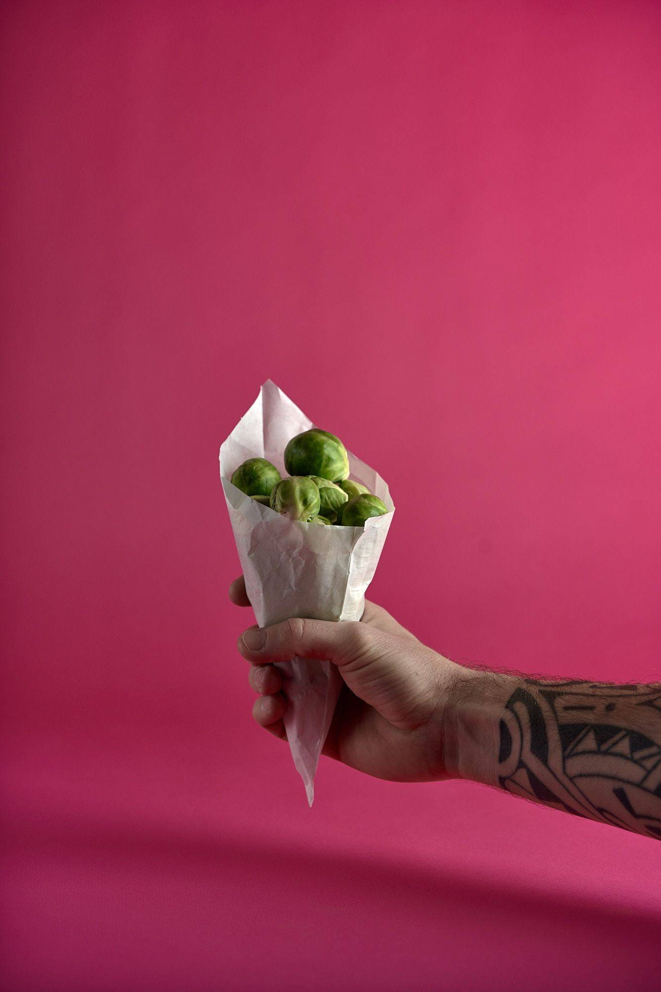 brussels-sprouts hand holding a paper bag with brussels sprouts on pink background