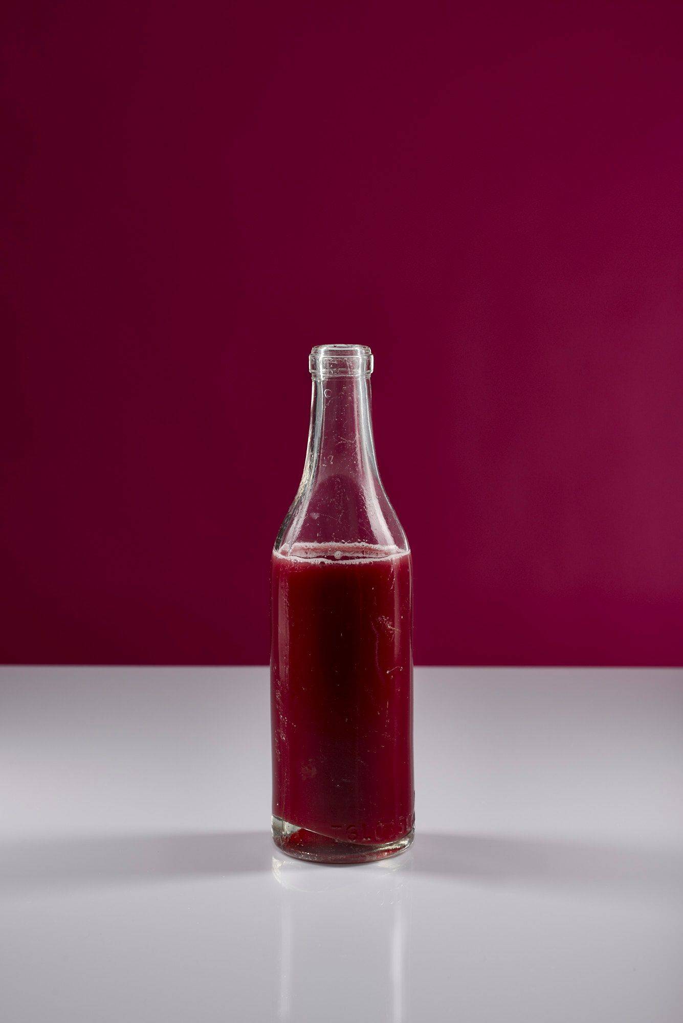 pomegranate-juice a glass bottle of pomegranate juice with white and pink background