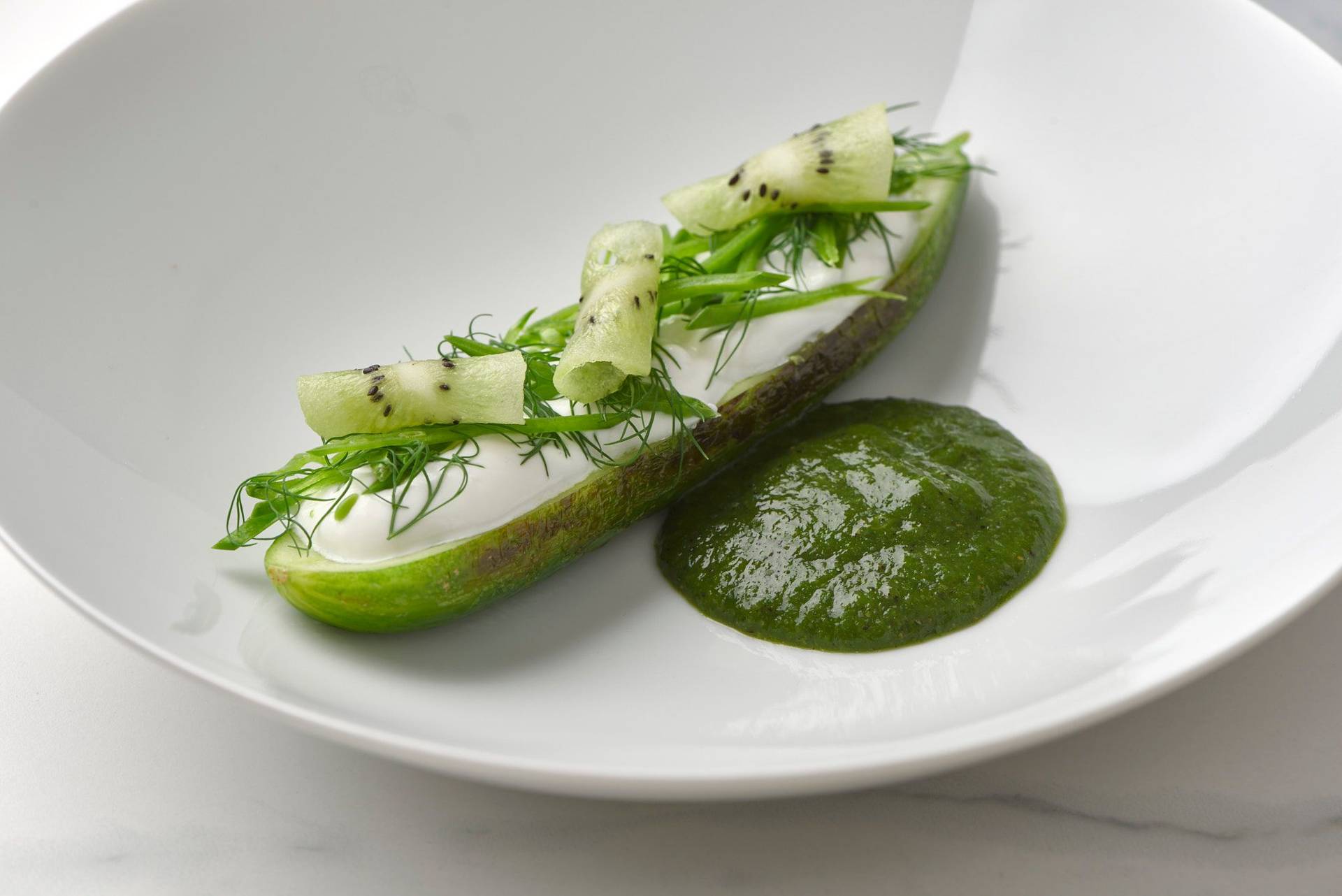 charred-cucumber-with-kiwi-salsa-skyr-and-dill charred cucumber with kiwi salsa skyr and dill on a white plate with a marbled sapienstone top