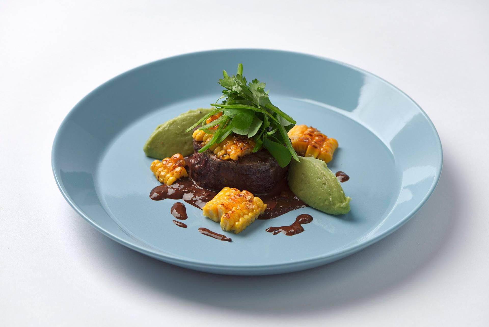 beef-steak-with-dark-beer-mole-sauce-corn-and-guacamole beef steak with dark beer mole sauce corn and guacamole on a blue plate with white background