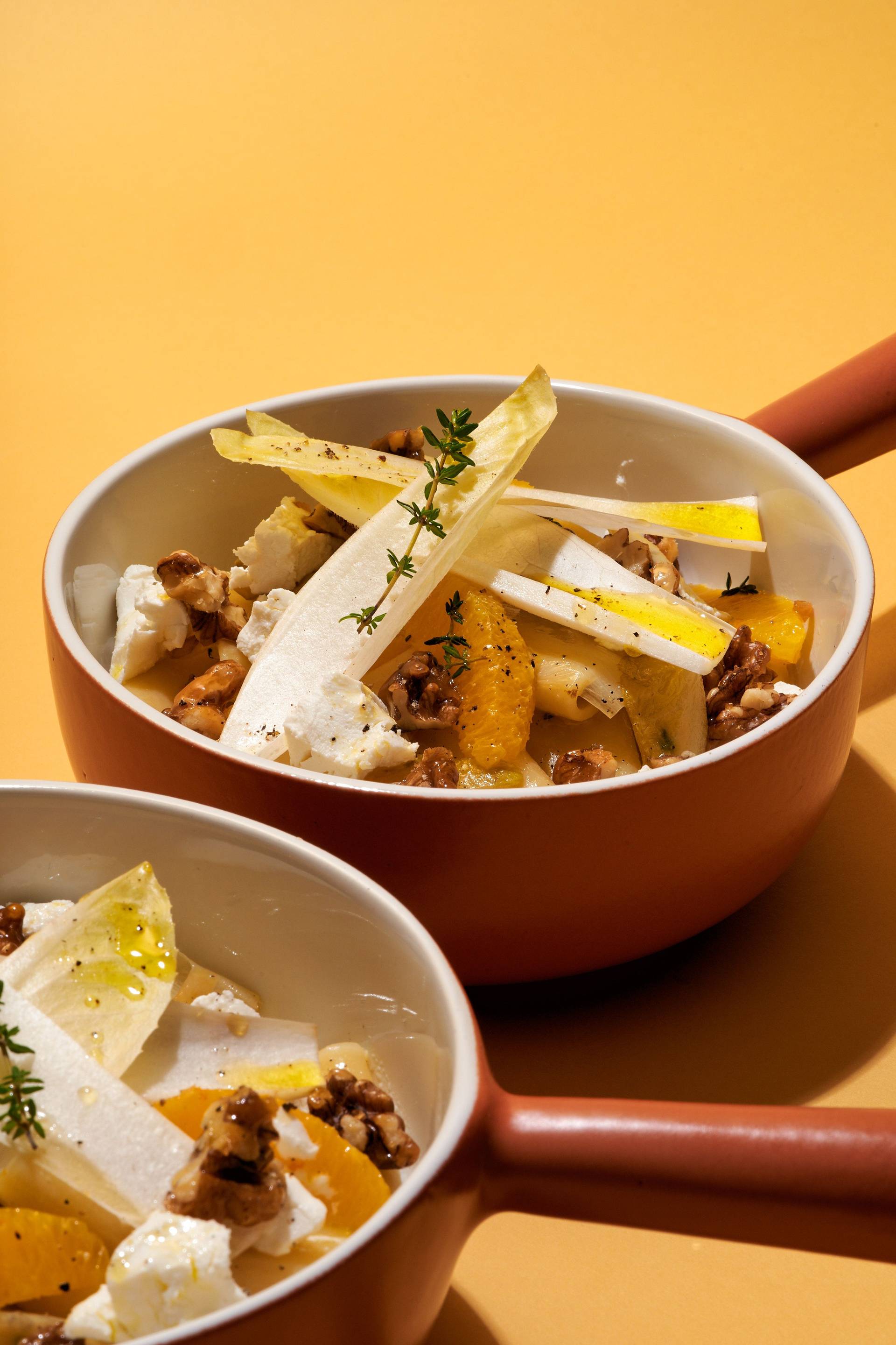 vegetarian-one-pot-pasta-with-chicory-orange-goat-cheese-and-candied-walnuts two bowls of vegetarian one pot pasta with chicory, orange, goat cheese and candied walnuts on yellow background