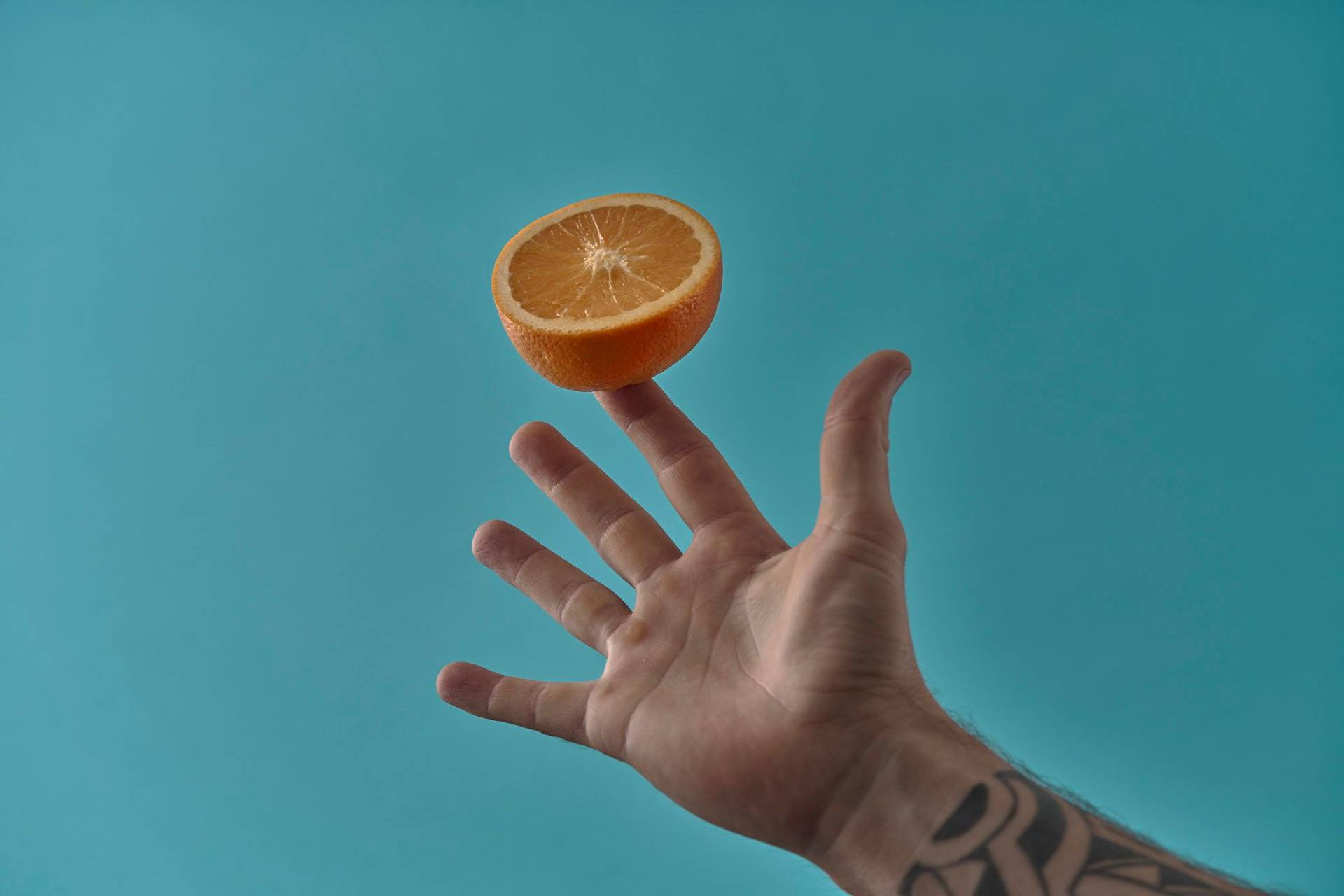 orange hand holding an orange on blue background
