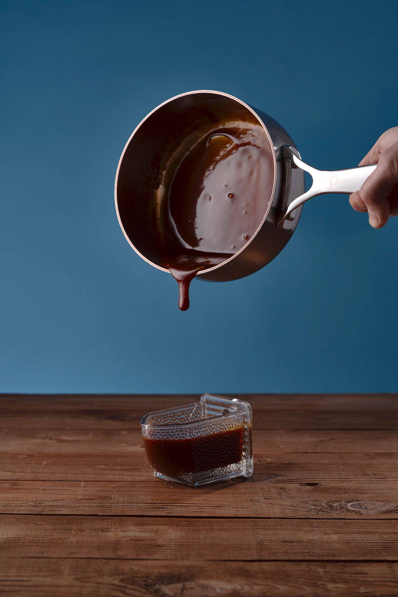 salted-caramel pouring salted caramel into vintage jar on a wooden table with blue background
