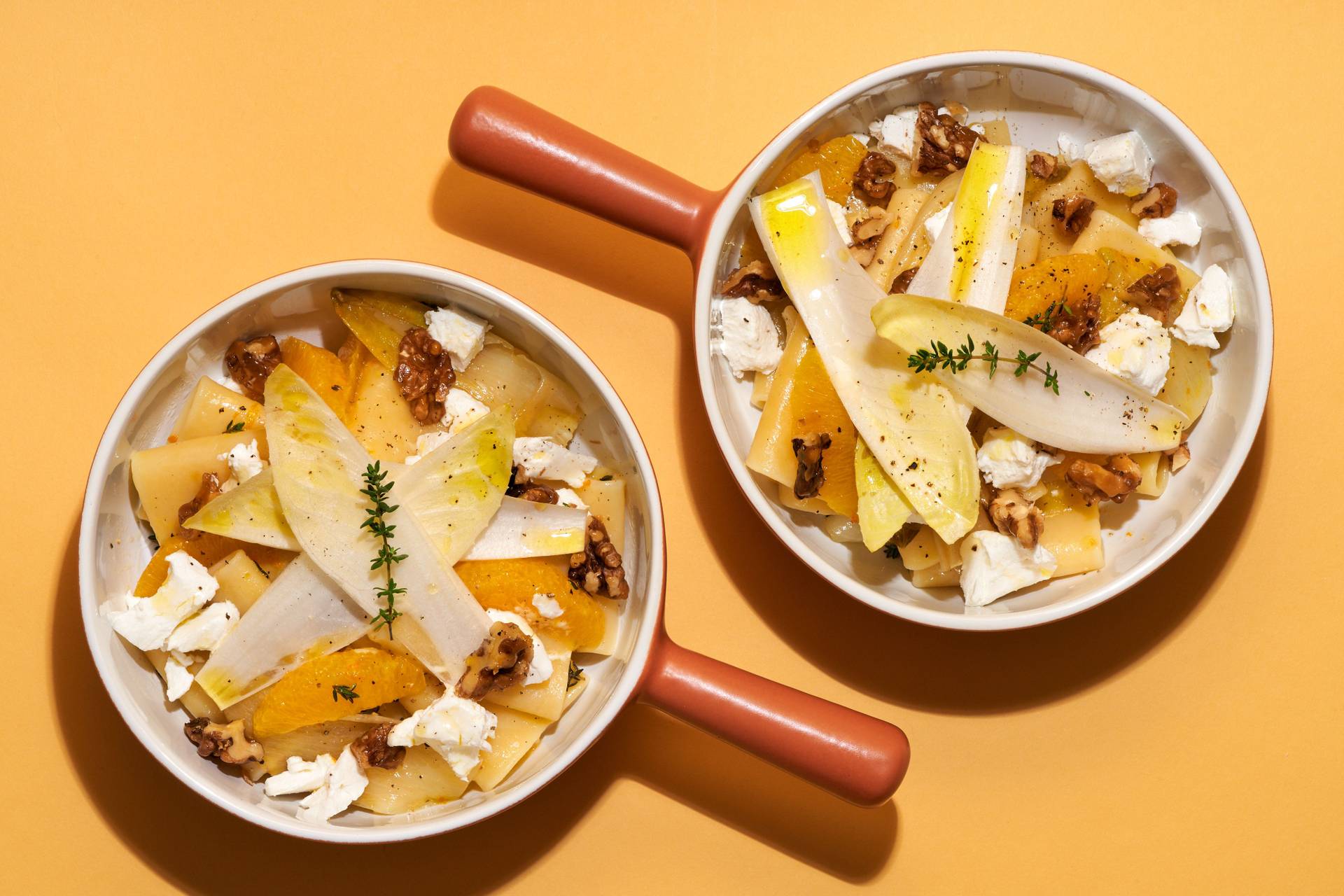 vegetarian-one-pot-pasta-with-chicory-orange-goat-cheese-and-candied-walnuts top shot of two bowls of vegetarian one pot pasta with chicory, orange, goat cheese and candied walnuts on yellow background