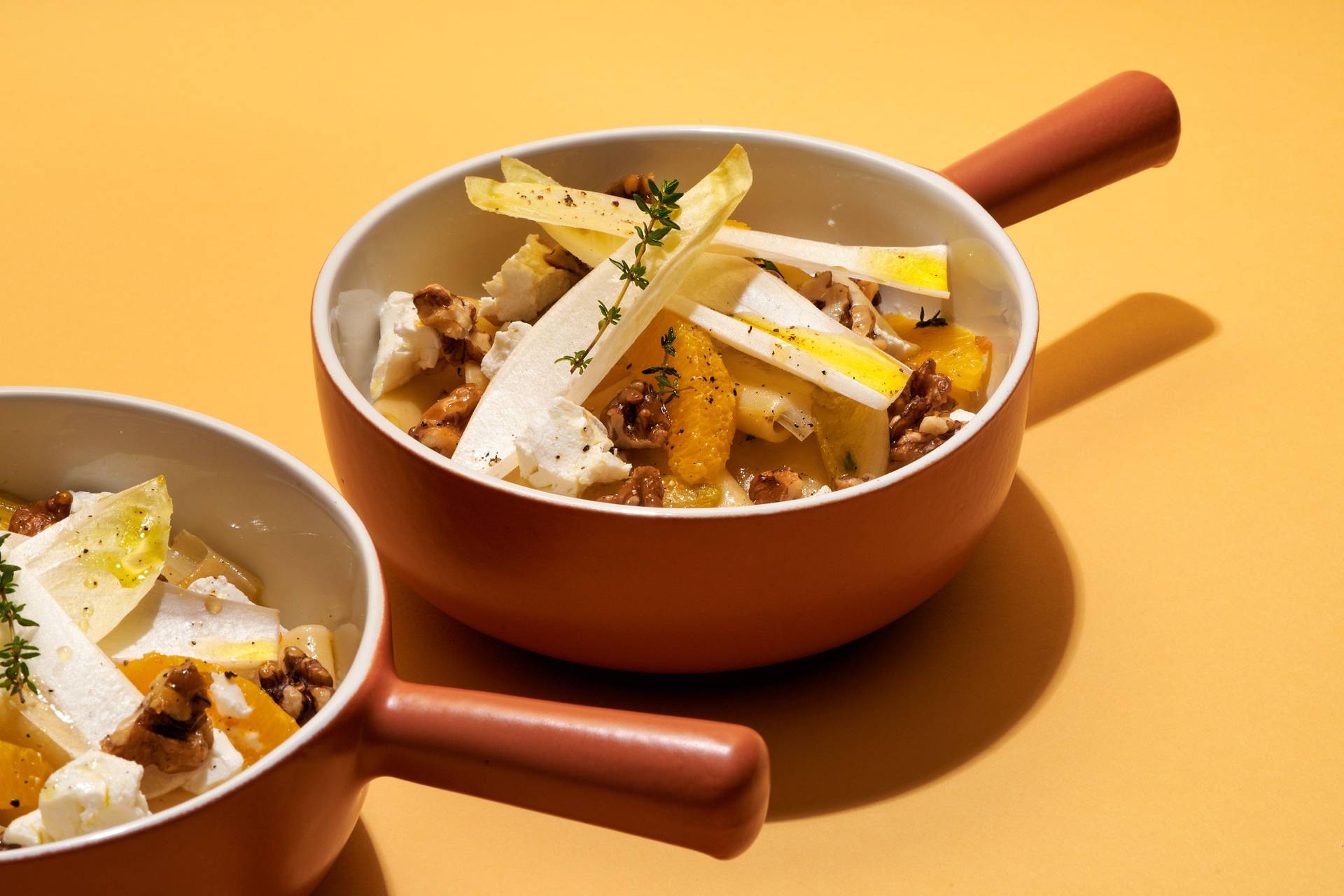 vegetarian-one-pot-pasta-with-chicory-orange-goat-cheese-and-candied-walnuts two bowls of vegetarian one pot pasta with chicory, orange, goat cheese and candied walnuts on yellow background