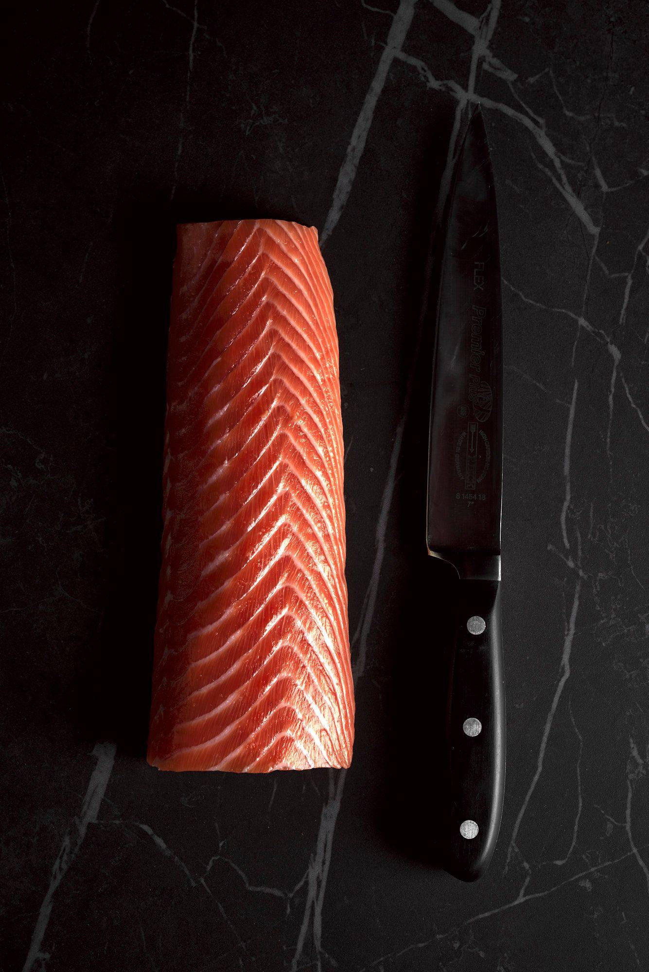 salmon-loin a raw salmon loin with a kitchen knife on a gray sapienstone top